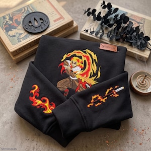 May include: A black sweatshirt featuring detailed embroidery of an anime character with spiky yellow and red hair surrounded by flames. The sleeves display additional flame embroidery and a sword design. A small brown leather tag reads Stitchales.