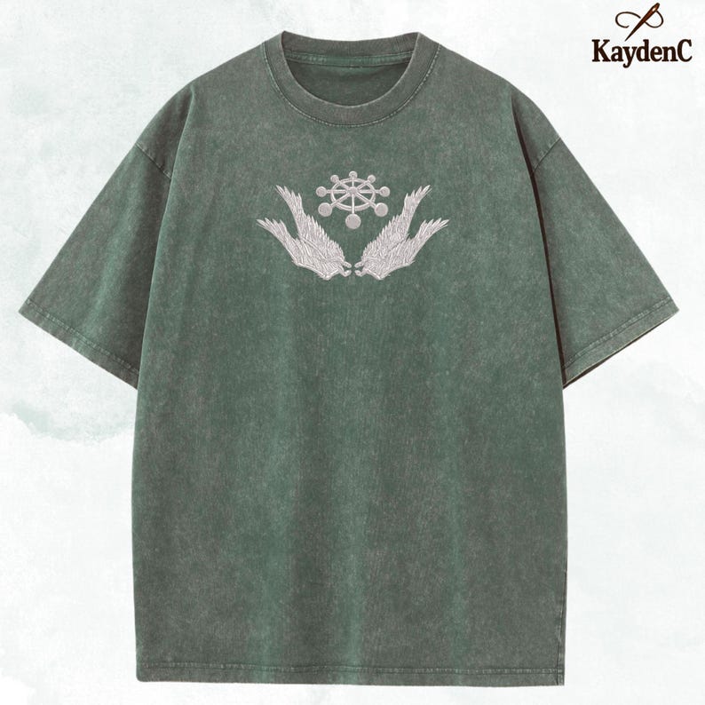 May include: Green short-sleeved t-shirt with a crew neck. The shirt features a white embroidered design of a wheel-like shape above two stylized wings. The brand name "KaydenC" is printed in white on the upper right corner.