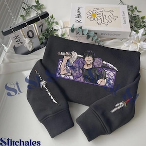 Peut inclure: Un sweat-shirt noir à manches longues avec une impression graphique d'un personnage aux cheveux sombres portant une épée sur la poitrine. Les manches sont ornées d'illustrations d'épées individuelles, une de chaque côté, sur fond sombre.