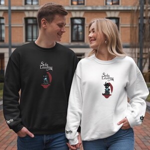 May include: Two people wearing black and white sweatshirts with the text "Solo Leveling" and a graphic of a character from the anime. The sweatshirts have the word "igris" on the cuffs.