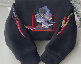 May include: A black hooded sweatshirt featuring a central embroidered graphic of a character with blue hair holding a sword inside a red square frame. Each sleeve displays an embroidered red and gold sword design with intricate detailing.