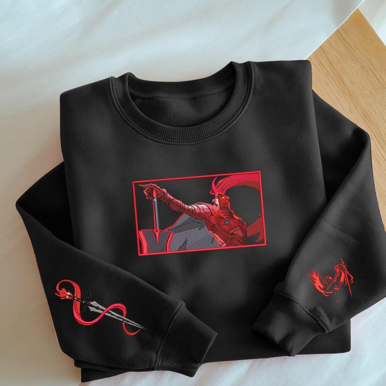 Puede incluir: Sudadera negra con un dise&ntilde;o gr&aacute;fico rojo y gris de un guerrero se&ntilde;alando con una espada. El dise&ntilde;o est&aacute; enmarcado en un rect&aacute;ngulo rojo. Gr&aacute;ficos rojos adicionales de una lanza y un guerrero en las mangas.