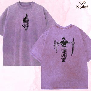 Puede incluir: Dos camisetas lavanda con dise&ntilde;os gr&aacute;ficos negros. Una camiseta presenta una cara estilizada y una espada, la otra una figura con armas. Las camisetas tienen un aspecto vintage texturizado. El logotipo de KaydenC est&aacute; en la esquina superior derecha.