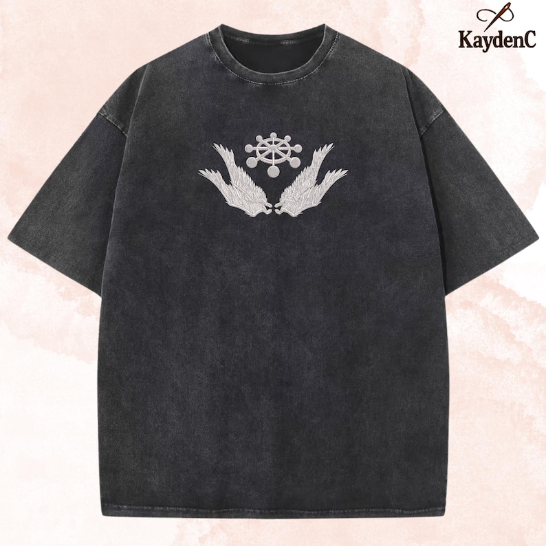 May include: Dark grey t-shirt with a white embroidered design of a central circular motif and stylized wings. The shirt has a vintage, washed look and a loose fit. The brand name "KaydenC" is visible in the upper right corner.