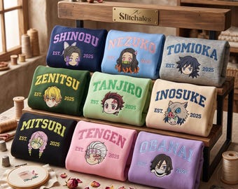 May include: A collection of nine folded sweatshirts in various colors, each featuring an embroidered anime character head, a name, and the text EST. 2025. The sweatshirts are displayed on a wooden rack with a brass plaque labeled Stitchales.