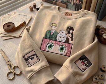 May include: A beige crewneck sweatshirt featuring embroidered anime-style character graphics. The chest displays a group of four characters, while each sleeve features a smaller square embroidery of a single eye. The interior neck label reads ST.