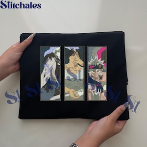 Puede incluir: Camiseta negra con tres paneles de personajes de estilo anime. Cada panel presenta un personaje diferente con rasgos y ropa detallados. El logotipo de Stitchales es visible en la parte superior izquierda.