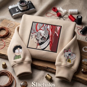 Könnte beinhalten: Ein beigefarbenes Sweatshirt mit einer großen, quadratischen Stickerei eines stilisierten Charakters mit weißem Haar, roten Akzenten und einer Maske. Die Ärmel zeigen kleinere Stickereien einer Person mit Brille und einer katzenartigen Figur.