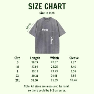 Puede incluir: Tabla de tallas para una camiseta gris, con medidas en pulgadas. La tabla incluye medidas de largo, ancho y manga para las tallas S, M, L, XL y 2XL. El texto indica que las tallas pueden variar en 1-2 cm.