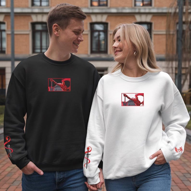 Puede incluir: Sudaderas negras y blancas con un dise&ntilde;o gr&aacute;fico rojo. Las sudaderas tienen un dise&ntilde;o rojo en la manga. Las sudaderas las lleva una pareja.