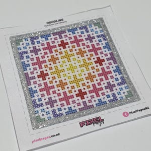 Puede incluir: Patrón de punto de cruz cuadrado con una combinación de colores arcoíris, con un diseño central amarillo que irradia hacia afuera a través del naranja, rosa, azul y morado. El diseño está enmarcado por un borde de purpurina plateada. El texto "DOODLING" y "Pixel Pages" son visibles.