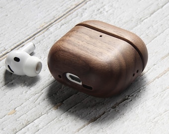 May include: A dark brown wooden protective case for wireless earbuds, featuring a smooth grain finish and a precise cutout for a charging port, positioned next to a single white wireless earbud with a black sensor and silicone tip.