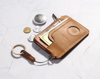 May include: A tan leather wallet with a zipper closure and a key ring attached. The wallet has a small pocket on the outside and a larger pocket on the inside. The wallet is lying on a white tiled surface.