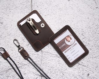 May include: A brown leather ID card holder with a metal clip and a matching lanyard. The holder displays an ID card with the name "Amanda Clark". The leather has a distressed finish.