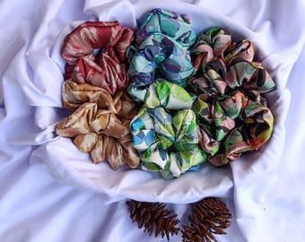 May include: A collection of colorful patterned hair scrunchies in a white bowl. The scrunchies are made of fabric and have a variety of floral and abstract designs.