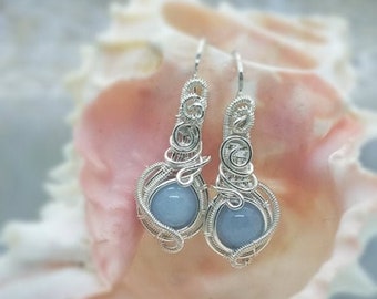 May include: A pair of silver wire wrapped earrings with light blue gemstone accents.