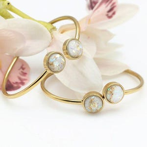 May include: Two gold bangle bracelets with white opal-like stones. The bracelets are delicate and have a simple design.