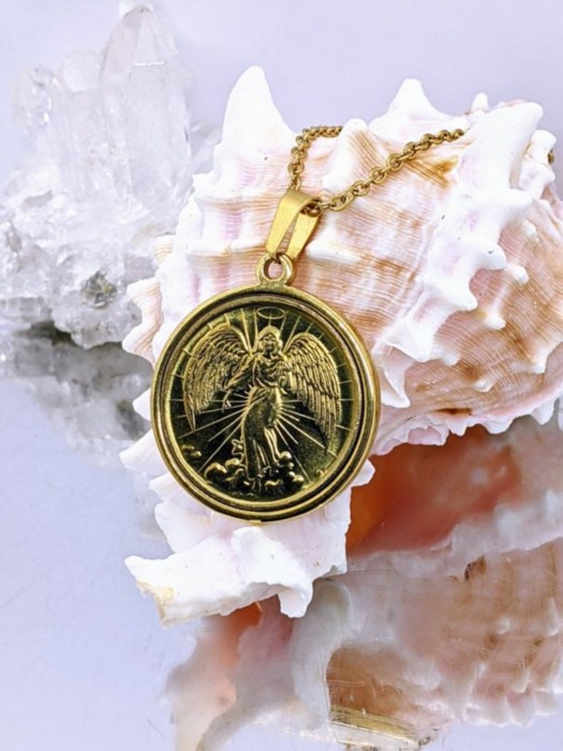 Puede incluir: Collar con colgante de oro que presenta un &aacute;ngel detallado con alas, sobre un fondo de nubes y rayos de luz. El colgante est&aacute; unido a una delicada cadena de oro.