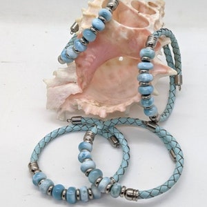 May include: Three blue leather bracelets with light blue gemstone beads and silver accents. The bracelets are stacked on top of each other.