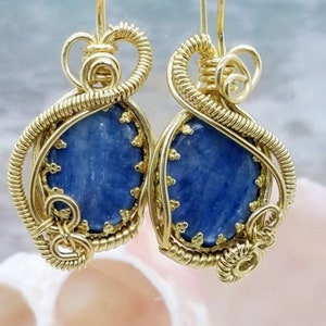 May include: Gold wire wrapped earrings with blue gemstone cabochons. The earrings are a delicate and intricate design.