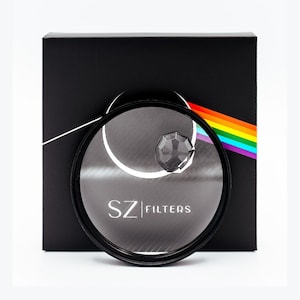 May include: A black box with a circular lens filter in front. The filter has the text "SZ FILTERS" printed on it. A clear, faceted crystal is in the center of the filter. A rainbow design is on the right side of the box.