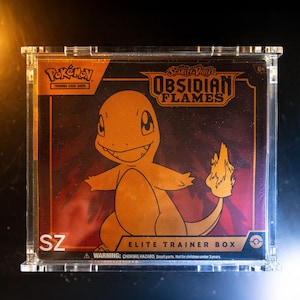 May include: A clear acrylic case contains a Pokémon trading card game box. The box features a gold Charmander illustration and the text "OBSIDIAN FLAMES". The box is labelled "ELITE TRAINER BOX" and includes a choking hazard warning.