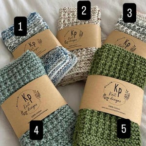 May include: Five folded knit washcloths in blue, beige, grey, sage green, and olive green, each wrapped in a brown paper band labeled Kp Knit designs 100% Cotton. The items are numbered one through five in black boxes on the image.