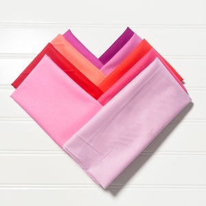 May include: A set of seven fabric squares in shades of pink and red, arranged in a heart shape. The squares are made of a soft, smooth fabric and are perfect for quilting, sewing, or crafting.