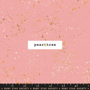 May include: A pink fabric featuring a scattered pattern of small white and gold paint-like splatters. A white rectangular label in the center displays the black text "peartree" with a small yellow pear icon. A black ruler measuring 7 inches is visible.