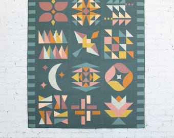 May include: A teal quilt with geometric patterns in shades of pink, orange, yellow, and white. The quilt features various shapes, including triangles, squares, and floral designs. The border has a striped pattern.