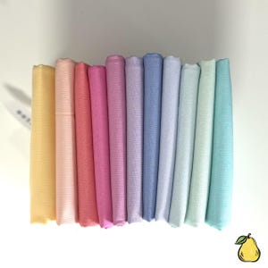 May include: A stack of folded fabric in a spectrum of pastel colors, including yellow, pink, red, purple, blue, and green. The fabric is neatly arranged, showcasing a variety of shades. The image is well-lit, highlighting the textures and hues of the textiles.