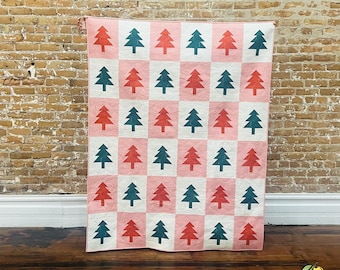 May include: A pink and white quilt with a repeating pattern of green and red Christmas trees.