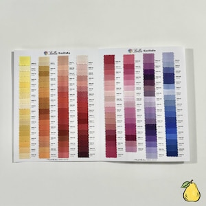 May include: Open book displaying a fabric color chart with the text "Bella Solids." The chart features numerous fabric swatches in a range of colors, from yellows and oranges to reds, pinks, purples, and blues. Each swatch is labeled with a unique number.