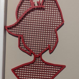 May include: Red metal wall decor in the shape of a person with a grid pattern. The decor is hanging on a wall with two white hooks.