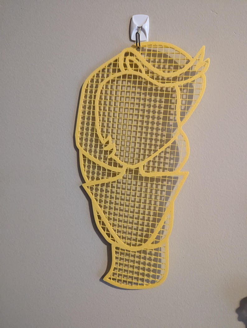 May include: A yellow, grid-like wall hanging in the shape of a person's head. The grid is made of small squares and the outline of the head is visible.