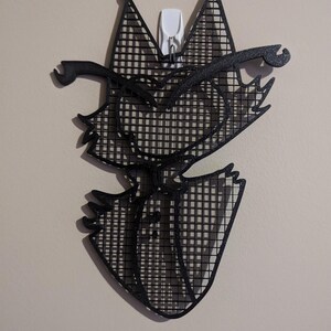May include: Black and white wall decor of a cartoon cat with a grid pattern. The cat has a mischievous expression and is wearing a hat.