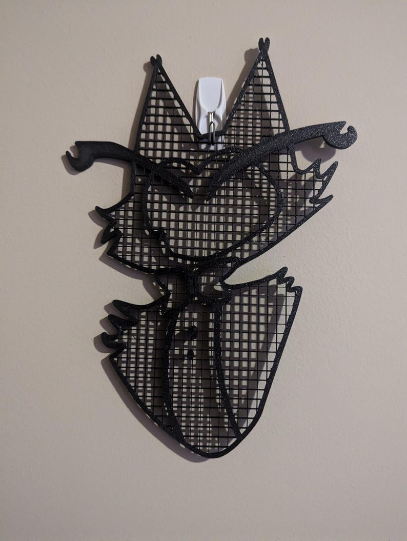 May include: Black and white wall decor of a cartoon cat with a grid pattern. The cat has a mischievous expression and is wearing a hat.