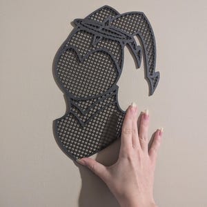 May include: A black and gray wall decor with a geometric design. The design is a silhouette of a person with a heart shape in the chest area. The decor is made of a material that looks like a mesh or a grid.