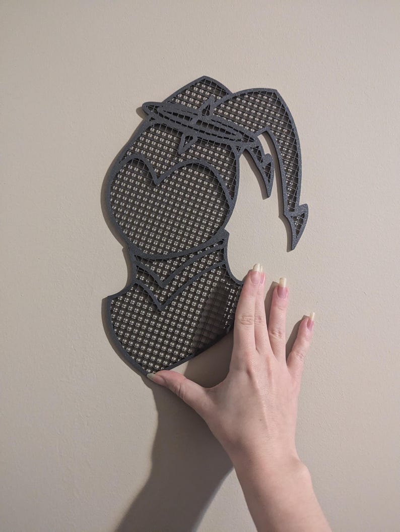 May include: A black and gray wall decor with a geometric design. The design is a silhouette of a person with a heart shape in the chest area. The decor is made of a material that looks like a mesh or a grid.