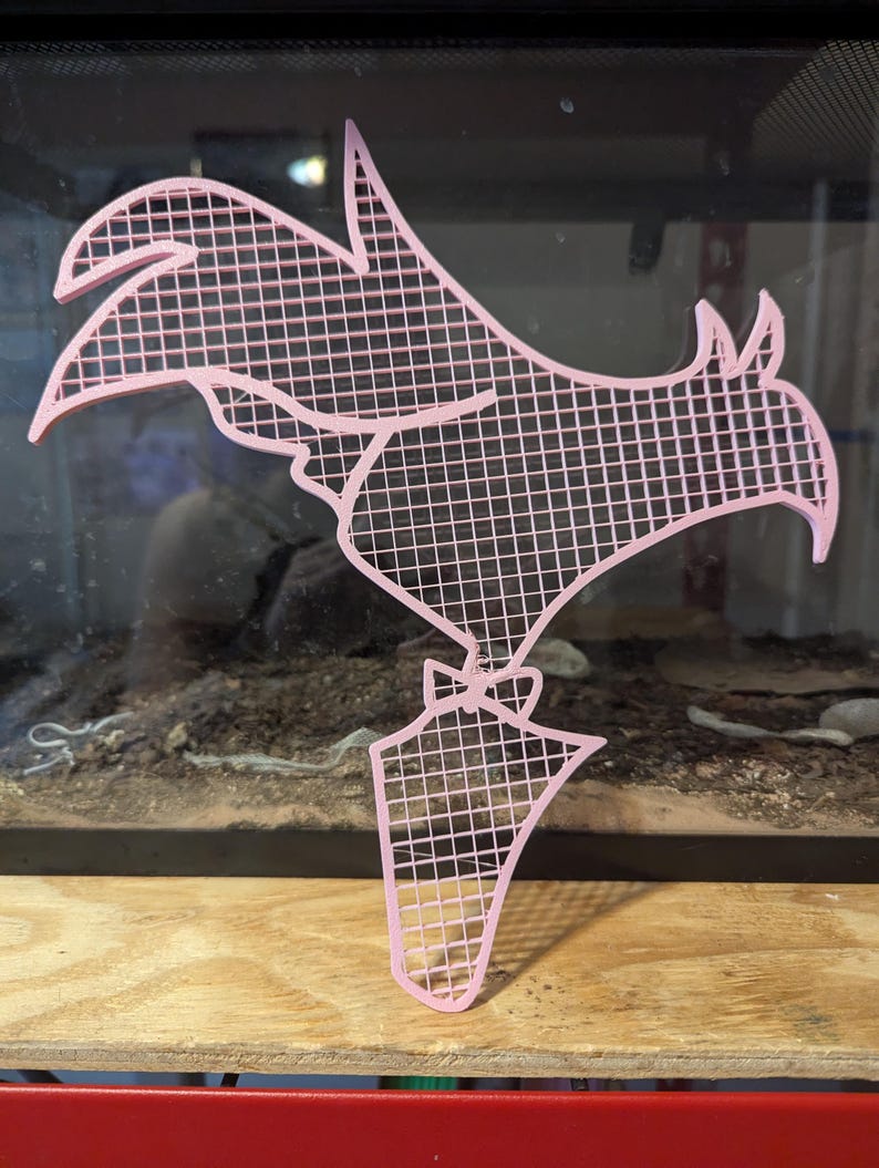 May include: A pink plastic rooster silhouette with a grid pattern. The rooster is standing on a small base.