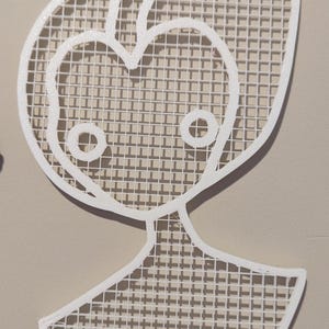 May include: White wall decor in the shape of a stylized person with a grid pattern. The decor is attached to the wall with two white hooks.