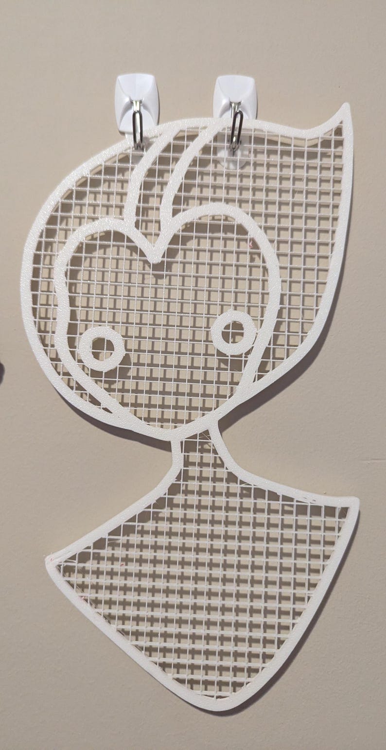 May include: White wall decor in the shape of a stylized person with a grid pattern. The decor is attached to the wall with two white hooks.