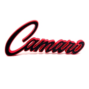 Peut inclure: Logo Camaro rouge et noir. Le mot "Camaro" est écrit en lettres cursives. Les lettres sont rouges avec un contour noir et un remplissage noir texturé, sur fond blanc.