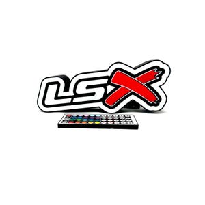 Könnte beinhalten: Schwarz-weißes LSX-Logo mit rotem X, begleitet von einer Fernbedienung mit farbigen Tasten. Das Logo ist schwarz-weiß umrandet, das X ist rot. Die Fernbedienung hat ein schwarzes Gehäuse.