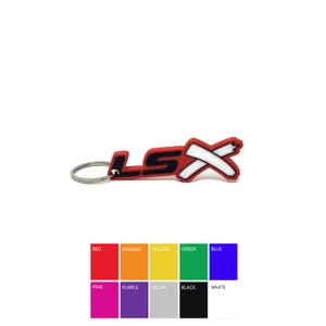 May include: A red, black, and white LSX keychain. The keychain features the letters "LSX" in a bold, stylized font. The "LSX" is red with black and white accents. The keychain has a silver metal ring.