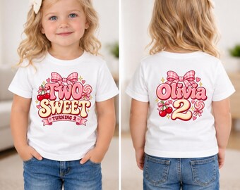 Könnte beinhalten: Ein weißes Kurzarm-T-Shirt mit einem Grafikdruck aus einer rosa Vichy-Schleife, Kirschen und einem Lutscher. Die Vorderseite zeigt den Text Two Sweet Turning 2, während auf der Rückseite der Name Olivia und die Zahl 2 in Rosa stehen.