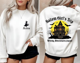 May include: White sweatshirt with a black witch silhouette and the name "Anna" printed on the front. The back features a haunted house graphic with the text "Salem Girl's Trip" and "Witchy Adventures Await".