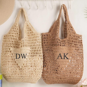 May include: Two woven tote bags in beige and brown hang against a white wall. The beige bag has the initials "DW" and the brown bag has "AK". A straw hat with the text "to be" is visible.