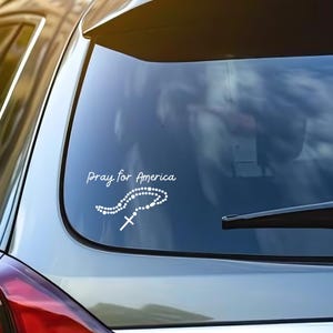 May include: A white vinyl sticker with the text "Pray for America" and a white image of a rosary with a cross.