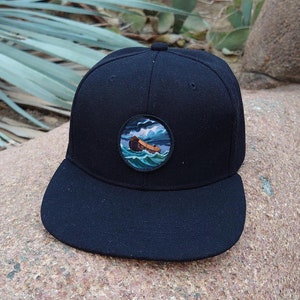 May include: Black baseball cap with a round embroidered patch depicting a boat in a stormy sea.